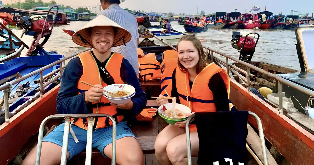 Enjoy a unique breakfast experience at Cai Rang Floating Market in the vibrant Mekong Delta. Tourists savor traditional Vietnamese noodles while sitting on a boat, surrounded by colorful vessels and lively river trading. This authentic moment highlights the cultural charm and local cuisine of Can Tho—a must-do activity for travelers exploring southern Vietnam.